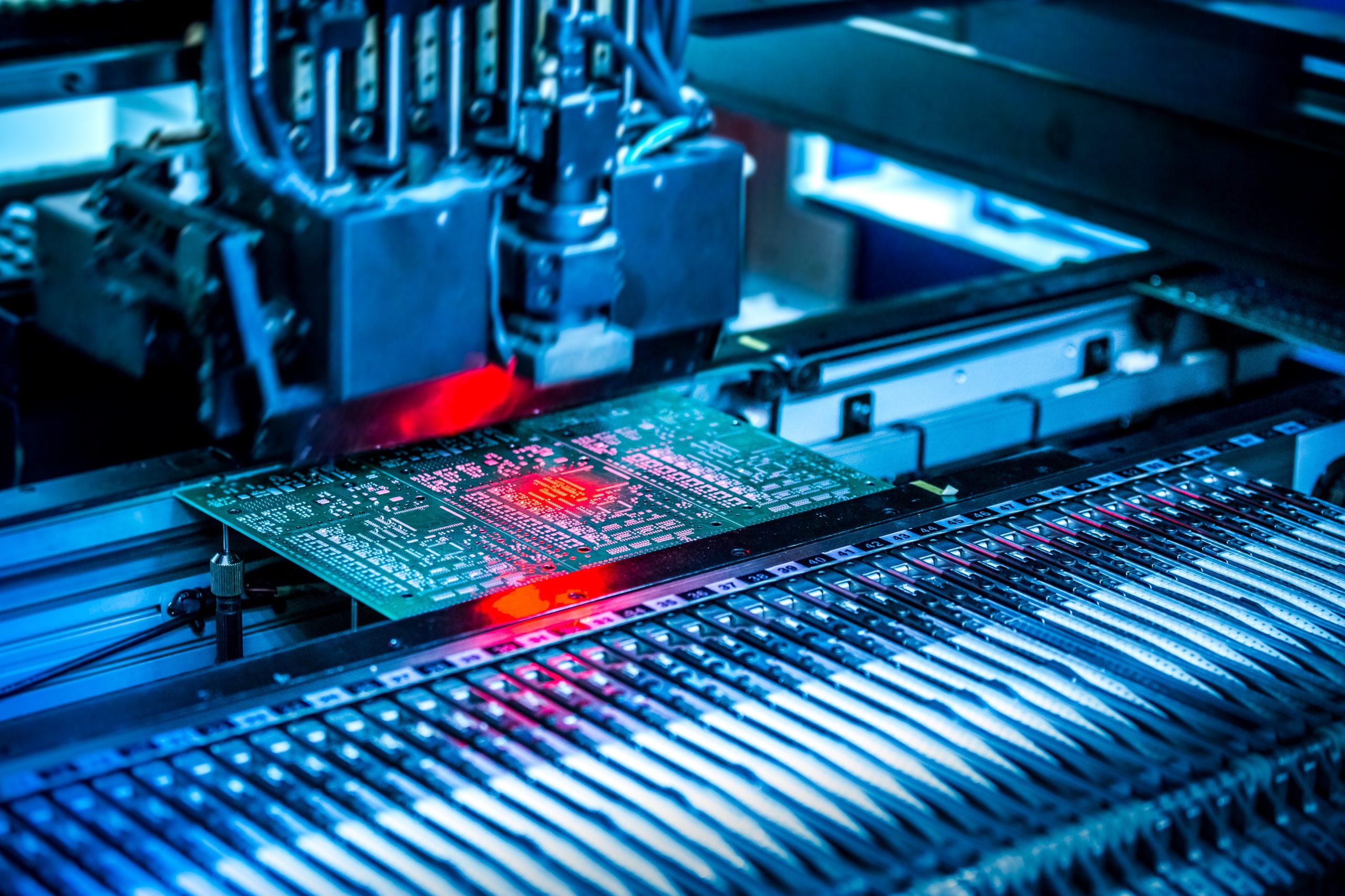 Electronic circuit under surface-mounting machine. Shot in red and blue tints. Surface-mount technology as a producing of electronic circuits. Components placed onto the surface of printed elements.