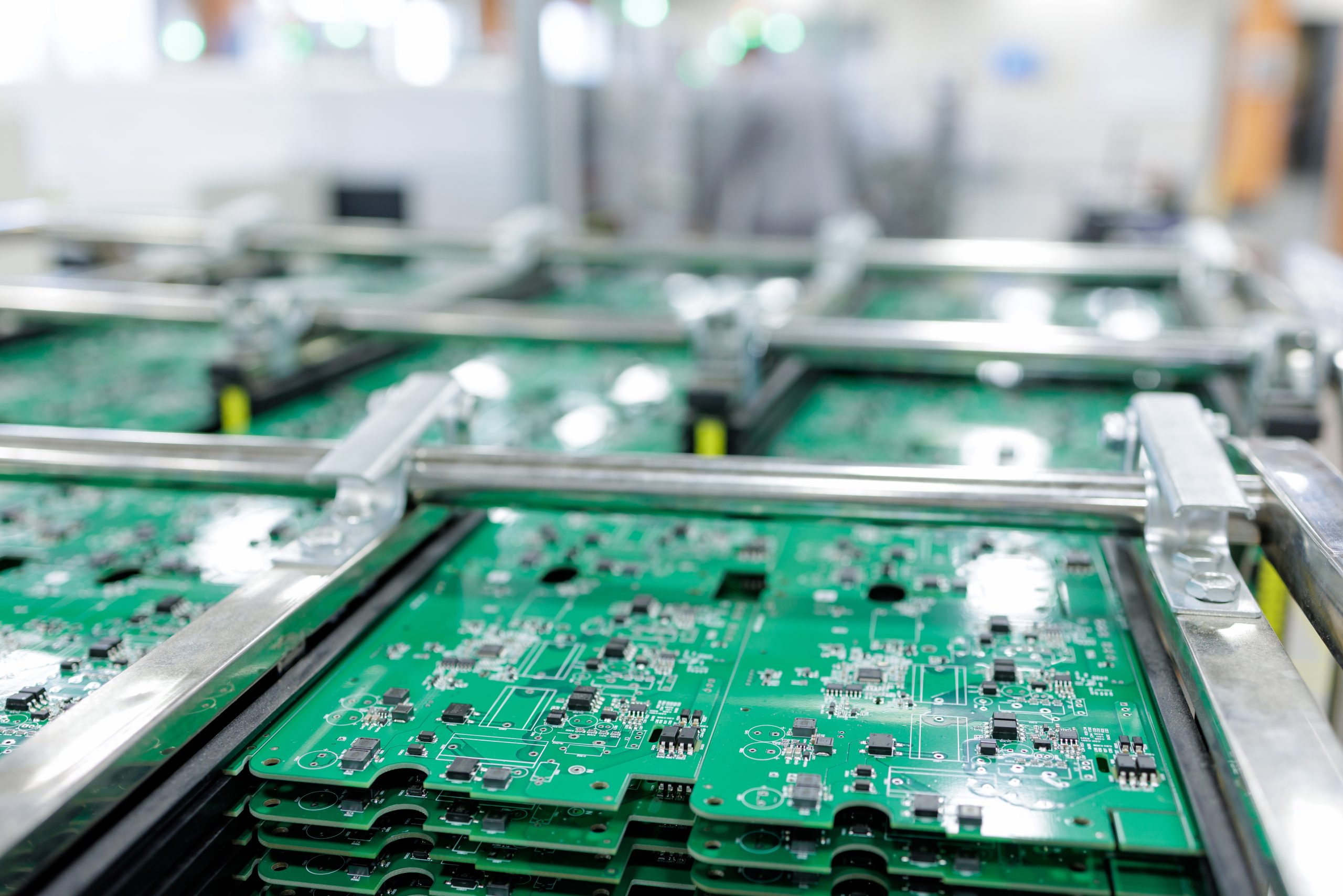 Stacks of assembled green printed circuit boards in metal rack on cart inside smart automated electronics factory
